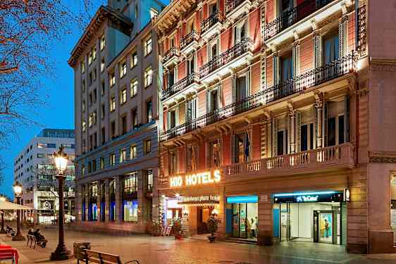 En bygade ved skumring med oplyste bygninger. Et hotelskilt lyser klart på facaden. (AI-genereret tekst)