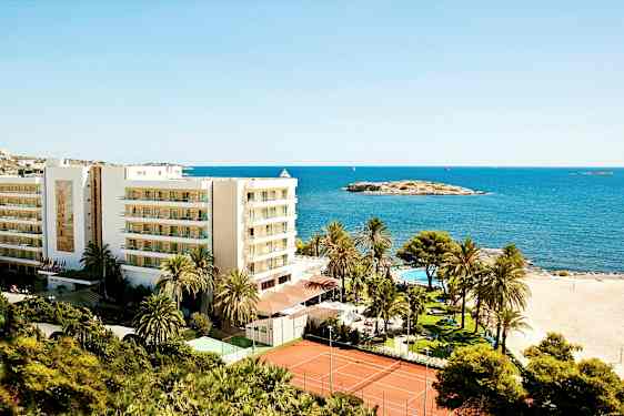 Billede af et feriested ved stranden med en bygning, palmer, swimmingpool og tennisbaner, placeret ved havet. (AI-genereret tekst)