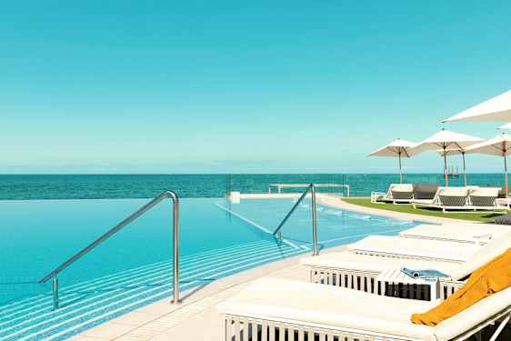 En infinitypool med udsigt over havet, omgivet af liggestole og parasoller. (AI-genereret tekst)