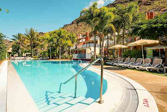 Udendørs pool med liggestole ved et hotel, omgivet af palmer og grønne planter. (AI-genereret tekst)