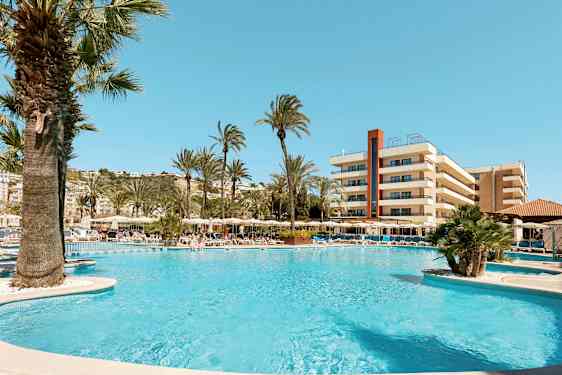 Billede af et poolområde med liggestole, parasoller og palmer foran et hotel. (AI-genereret tekst)