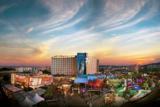 En udsigt over et feriehotel med en farverig temapark foran en solnedgang. (AI-genereret tekst)