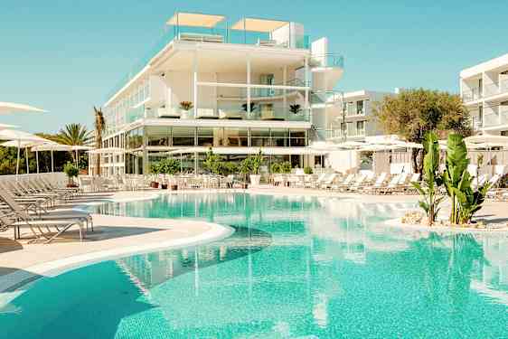 Et moderne hotel med glasaltaner ligger ved en klarblå pool omgivet af liggestole og grønne planter. (AI-genereret tekst)