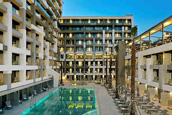 En moderne hotelbygning med altaner og en oplyst pool omgivet af liggestole. (AI-genereret tekst)