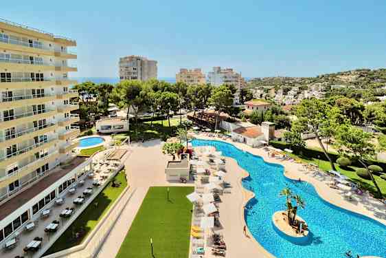 En hotelbygning ved siden af en pool med liggestole og parasoller samt omkringliggende beplantning og udsigt over en by. (AI-genereret tekst)