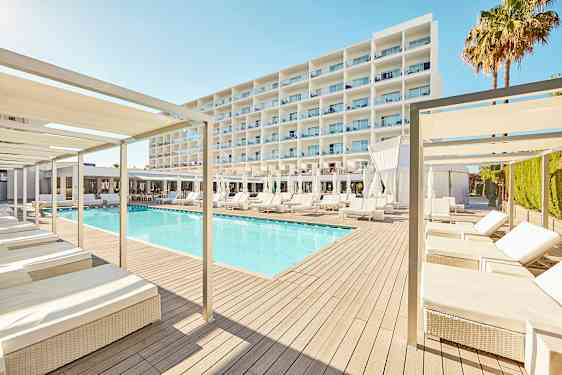 Et moderne hotelldesign med en pool omgivet af liggestole og parasoller, med en stor hvid bygning i baggrunden. (AI-genereret tekst)