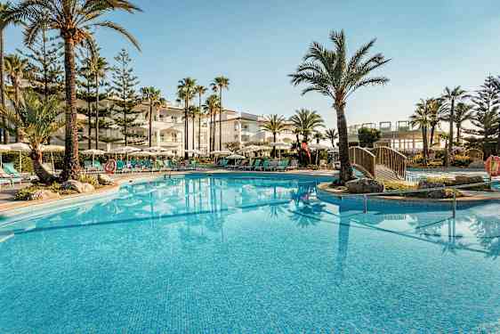 En udendørs pool omgivet af liggestole, parasoller og palmer ved et hotel. (AI-genereret tekst)