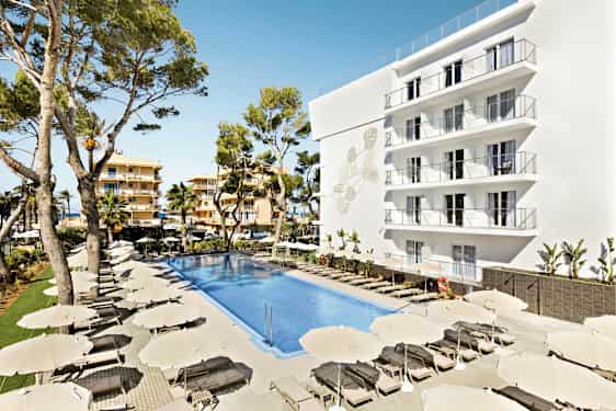 Billede af et hotelområde med en stor pool omgivet af solsenge og parasoller. En hvid bygning med flere altaner samt træer i baggrunden. (AI-genereret tekst)