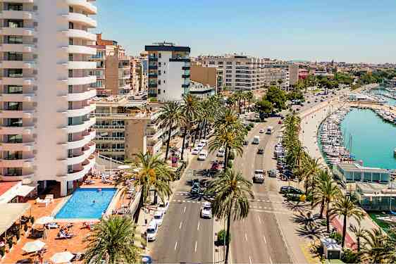 Billede der viser en vej med palmetræer, en pool ved en bygningskompleks og en havn med både. (AI-genereret tekst)