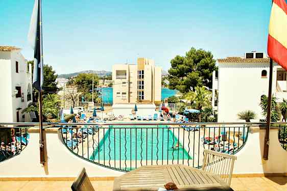 En pool med liggestole omkring og bygninger samt træer i baggrunden. (AI-genereret tekst)