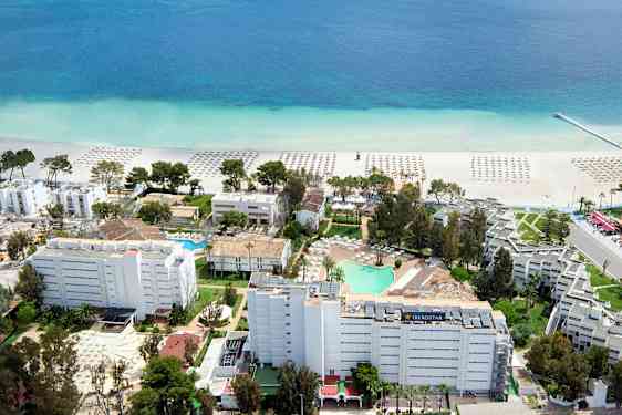 Luftfoto af et hotelområde nær stranden med parasoller på sanden og en klar blå havudsigt. (AI-genereret tekst)