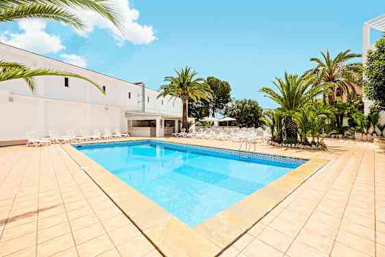 Billede, der viser en swimmingpool med lyseblåt vand, omgivet af en solterrasse med liggestole og palmer. (AI-genereret tekst)