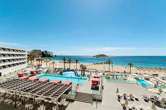 Billede af en solrig strand med palmer, turkis vand og en pool i forgrunden. Bygninger ses til venstre. (AI-genereret tekst)