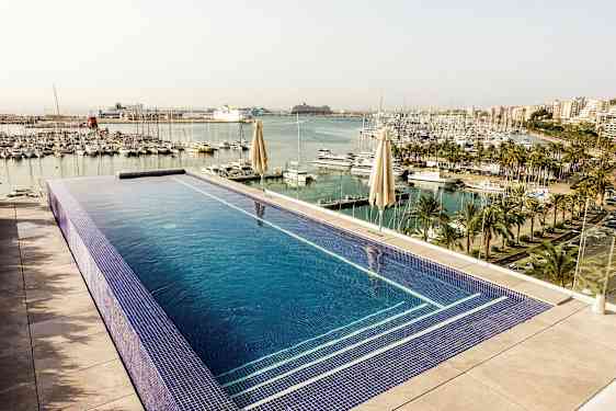 Billede af en infinitypool med udsigt over en lystbådehavn med palmer og fleretagers bygninger i baggrunden. (AI-genereret tekst)