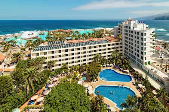 Hotelkompleks med pools og grønne områder tæt ved havet. (AI-genereret tekst)