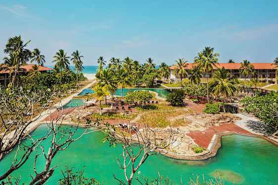 Hotelanlæg med pools, palmer og en sandstrand i baggrunden. (AI-genereret tekst)