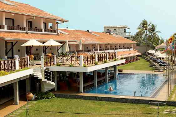 Hotel med udendørs pool, terrasser og liggestole. En person svømmer i poolen. (AI-genereret tekst)