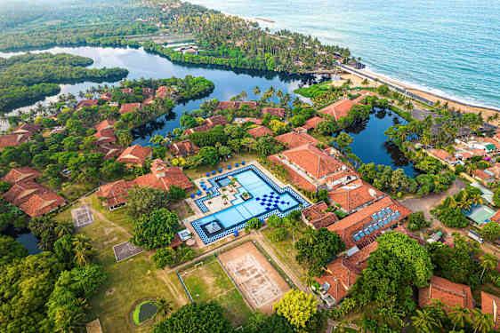 Luftfoto af en ferieby med terrakottafarvede tage, en stor swimmingpool og grønne omgivelser. (AI-genereret tekst)