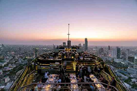 Tagterrasse ved solnedgang med restaurantgæster og panoramaudsigt over byens skyline. (AI-genereret tekst)