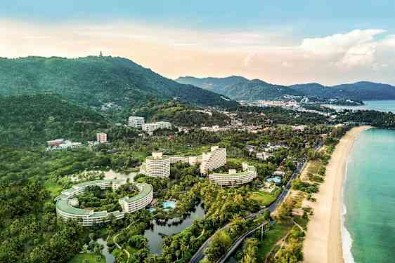 Luftfoto af et kystområde med hotelbygninger, omgivelser med grønt og en strand. (AI-genereret tekst)