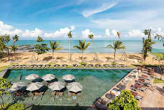 En strand med palmer i baggrunden og en pool med liggestole og parasoller i forgrunden. (AI-genereret tekst)