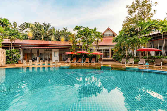 En pool med klart blåt vand, omgivet af liggestole med røde parasoller og grønne palmer i baggrunden. (AI-genereret tekst)