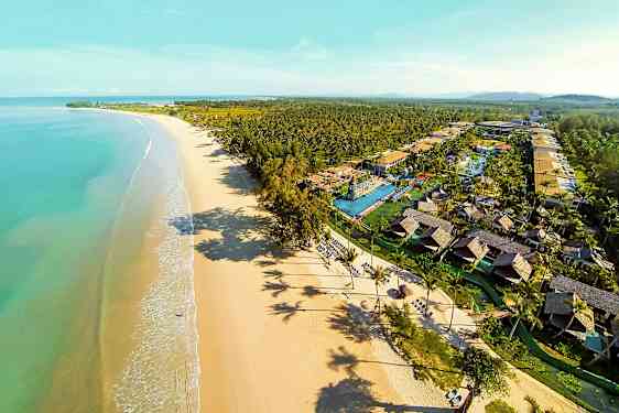Luftfoto af en lang sandstrand med turkis vand og et feriekompleks med bungalower og pools. (AI-genereret tekst)