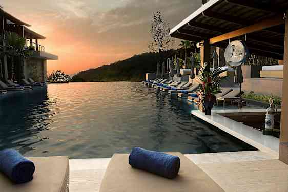 En infinitypool med solsenge og håndklæder på en ferieresort ved solnedgang. (AI-genereret tekst)