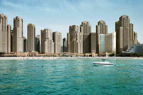 En strandlinje med høje bygninger i baggrunden og en båd på havet. (AI-genereret tekst)