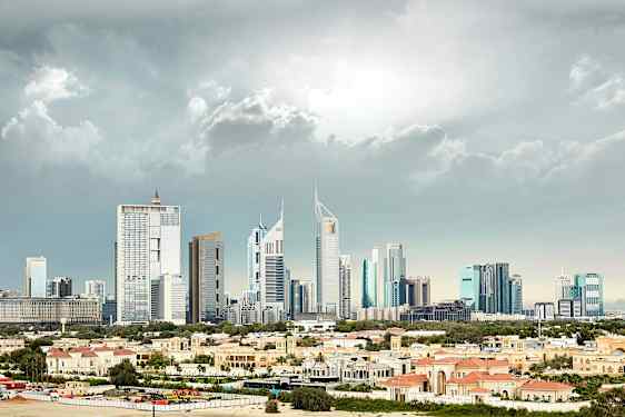 Billede af en by med høje, moderne bygninger i baggrunden og lave bygninger med rødlige tage i forgrunden. (AI-genereret tekst)