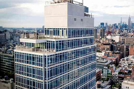 Høj bygning med glasfacade og terrasse, omgivet af bymiljø. (AI-genereret tekst)