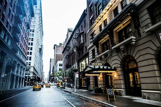 En bygade med høje bygninger langs siderne og taxaer, der kører på vejen. Evelyn Hotel-skiltet er synligt til højre. (AI-genereret tekst)