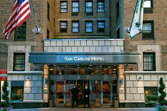 Indgangen til San Carlos Hotel, en bygning facade med mursten og flag. (AI-genereret tekst)