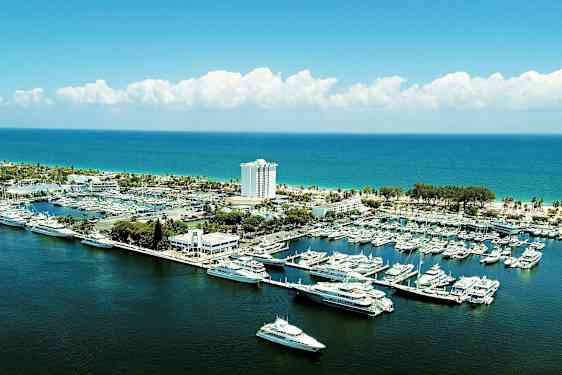 En marina med både og yachter ved kysten med en bygning og et hotel i baggrunden. (AI-genereret tekst)