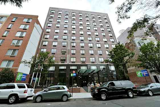 Et etagebyggeri med glasindgang og parkerede biler foran. (AI-genereret tekst)