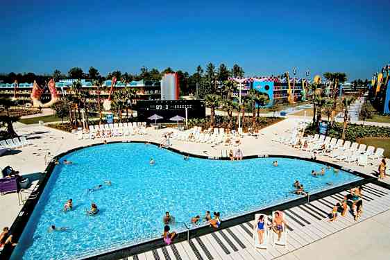 En swimmingpool omgivet af liggestole på et feriested. Baggrunden viser bygninger og dekorationer. (AI-genereret tekst)