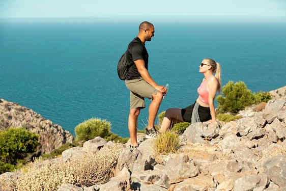 To personer holder en pause på en klippefyldt sti nær havet. (AI-genereret tekst)