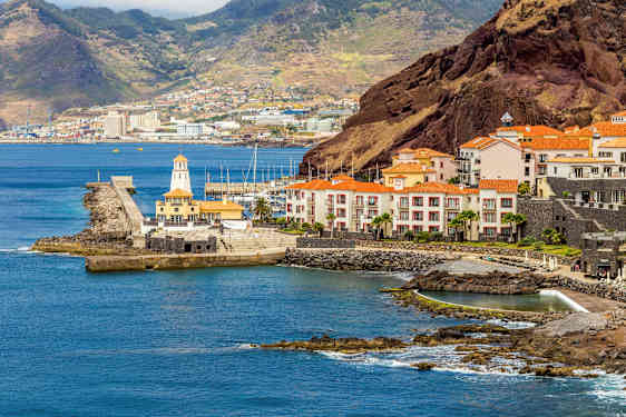 En kyst med bygninger med røde tage, en havn og bakker i baggrunden. (AI-genereret tekst)