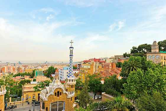 Udsigt over Park Güell i Barcelona med farverige bygninger og byens skyline i baggrunden. (AI-genereret tekst)