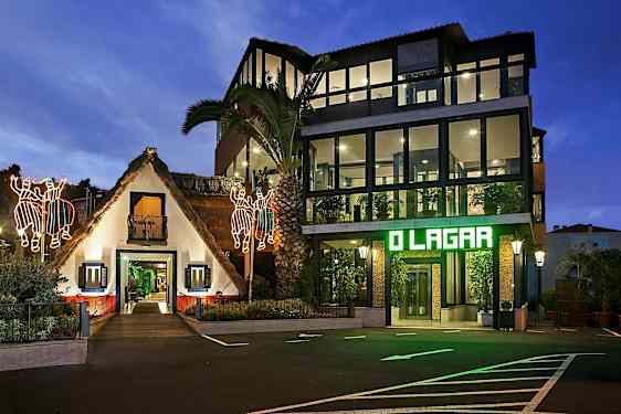 En bygning med en traditionel stråtækt struktur og en moderne glaspanelsbygning ved siden af, oplyst om aftenen med lysende dekorationer og belysning. (AI-genereret tekst)