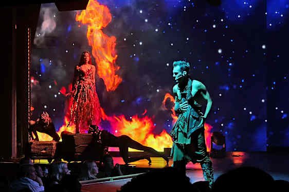 To personer optræder på en scene med ild og en stjernehimmel i baggrunden. (AI-genereret tekst)