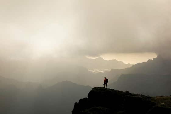 En vandrer står på en bjergtop med tågede dale og bjerge i baggrunden. (AI-genereret tekst)