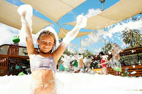 En gruppe mennesker nyder en aktivitet med skum under et skærmtag udendørs. (AI-genereret tekst)