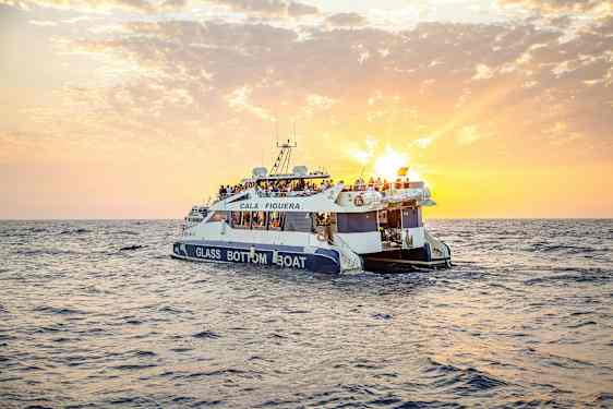 En glasbundsbåd med mennesker ombord sejler på havet under en solnedgang. (AI-genereret tekst)