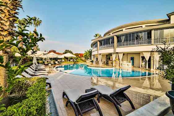 En udendørs pool omgivet af liggestole, parasoller og en moderne bygning. (AI-genereret tekst)