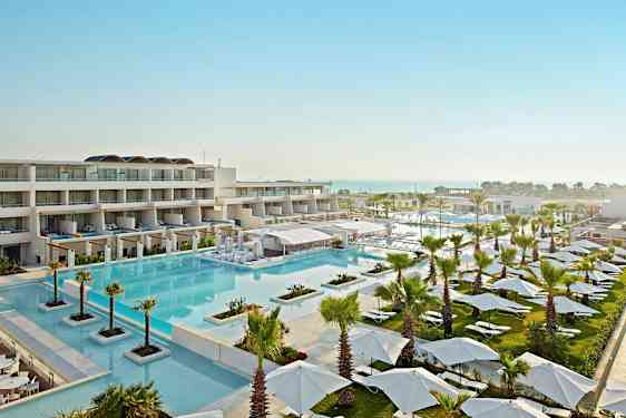 Udsigt over et moderne resort med en stor pool, liggestole, parasoller og bygninger. (AI-genereret tekst)