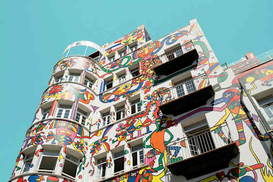 Bygning med farverige abstrakte malerier på facaden mod en klar blå himmel. (AI-genereret tekst)