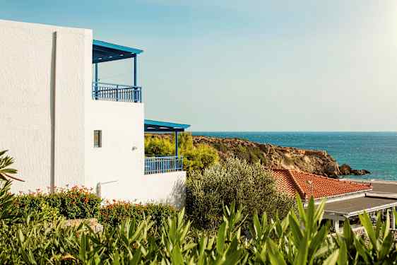 Hvid bygning med blå detaljer tæt på havet og grønne områder. (AI-genereret tekst)