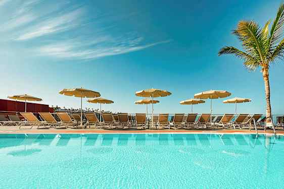 En pool med liggestole og parasoller under en klar blå himmel. (AI-genereret tekst)