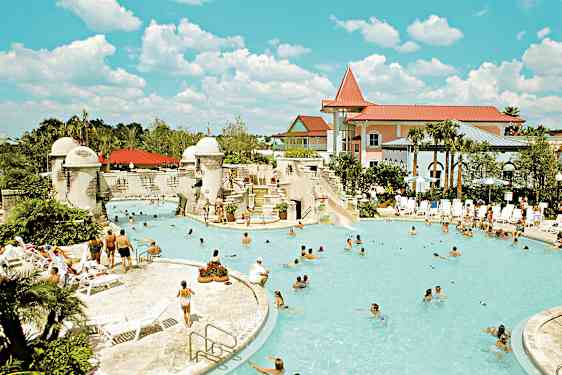 En udendørs pool omgivet af mennesker, liggestole og bygninger. (AI-genereret tekst)